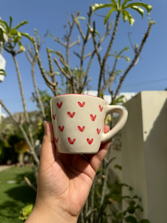 Small ceramic mug with tiny red hearts hand painted on the body with a red rim border. dimensions: 2.5" height 3" diameter